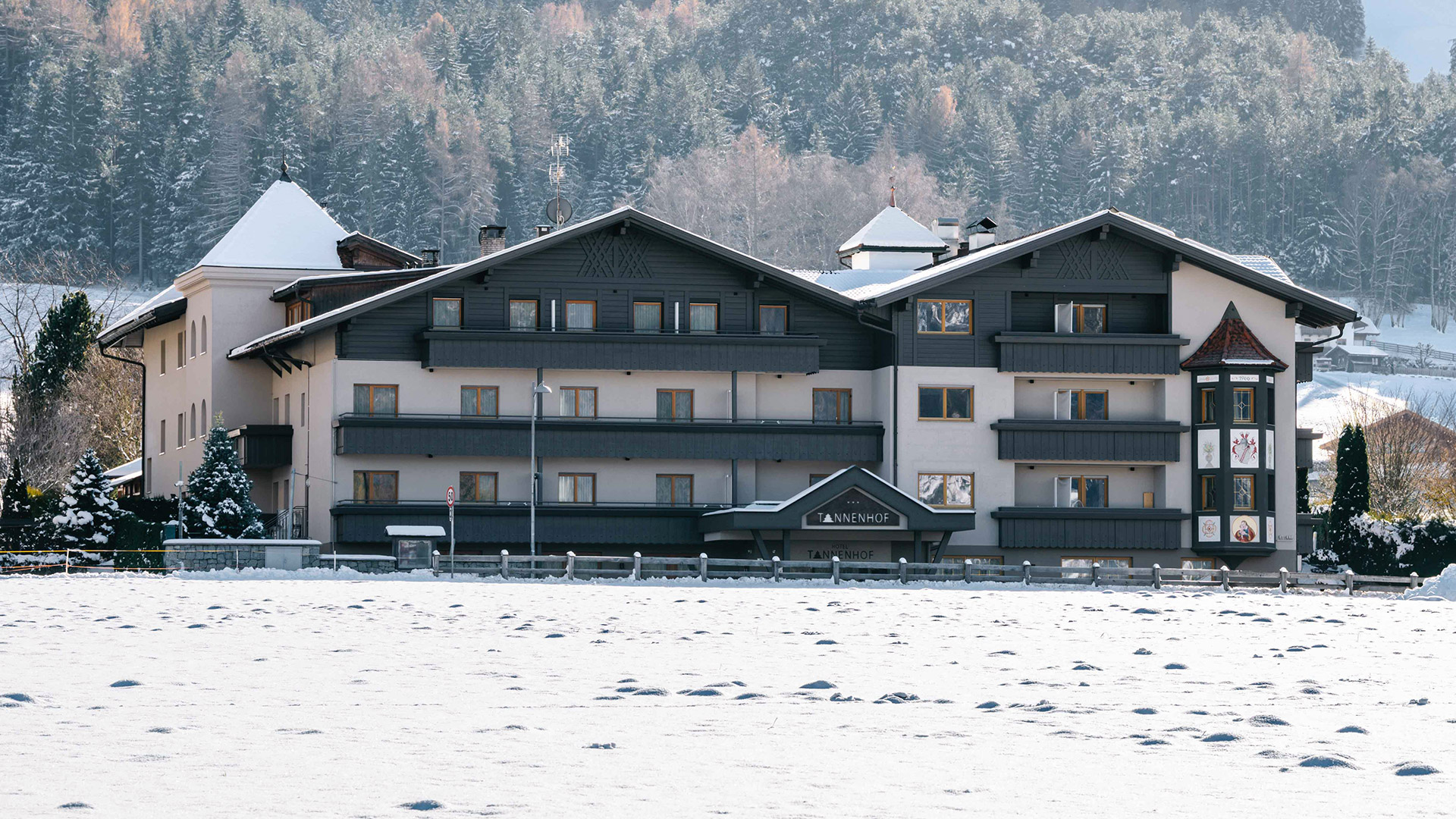 Das Hotel Tannenhof in Reischach am Kronplatz im Winter, umgeben von Schnee und Bergen.