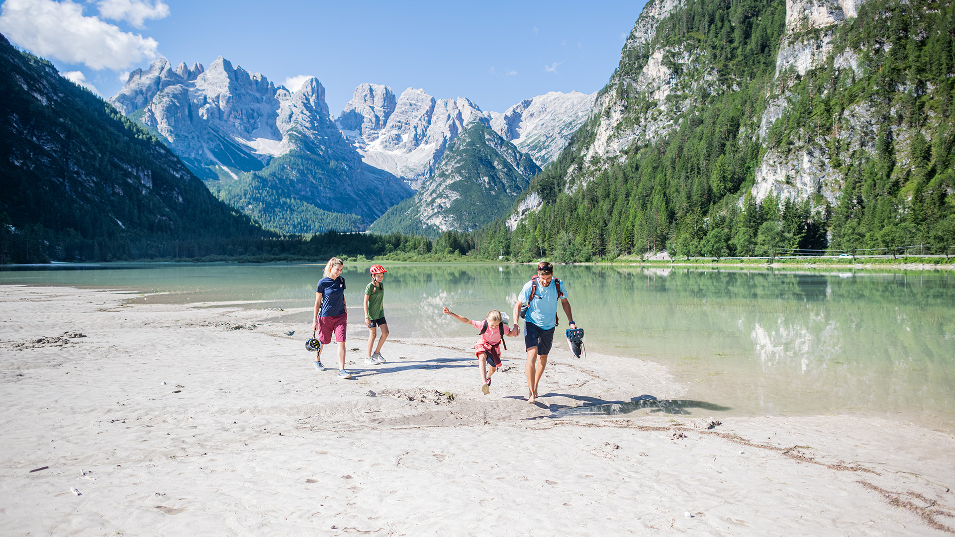 Famiglia sulla riva al Lago di Landro con le Dolomiti sullo sfondo, ideale per vacanze estive in Alto Adige.