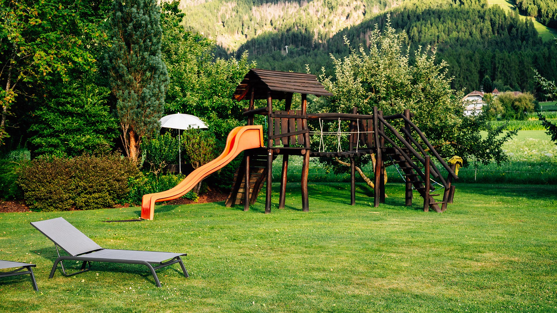 Ampio giardino dell'hotel con parco giochi (scivolo, torre da arrampicata) e sedie a sdraio per una rilassante vacanza in famiglia a Plan de Corones.