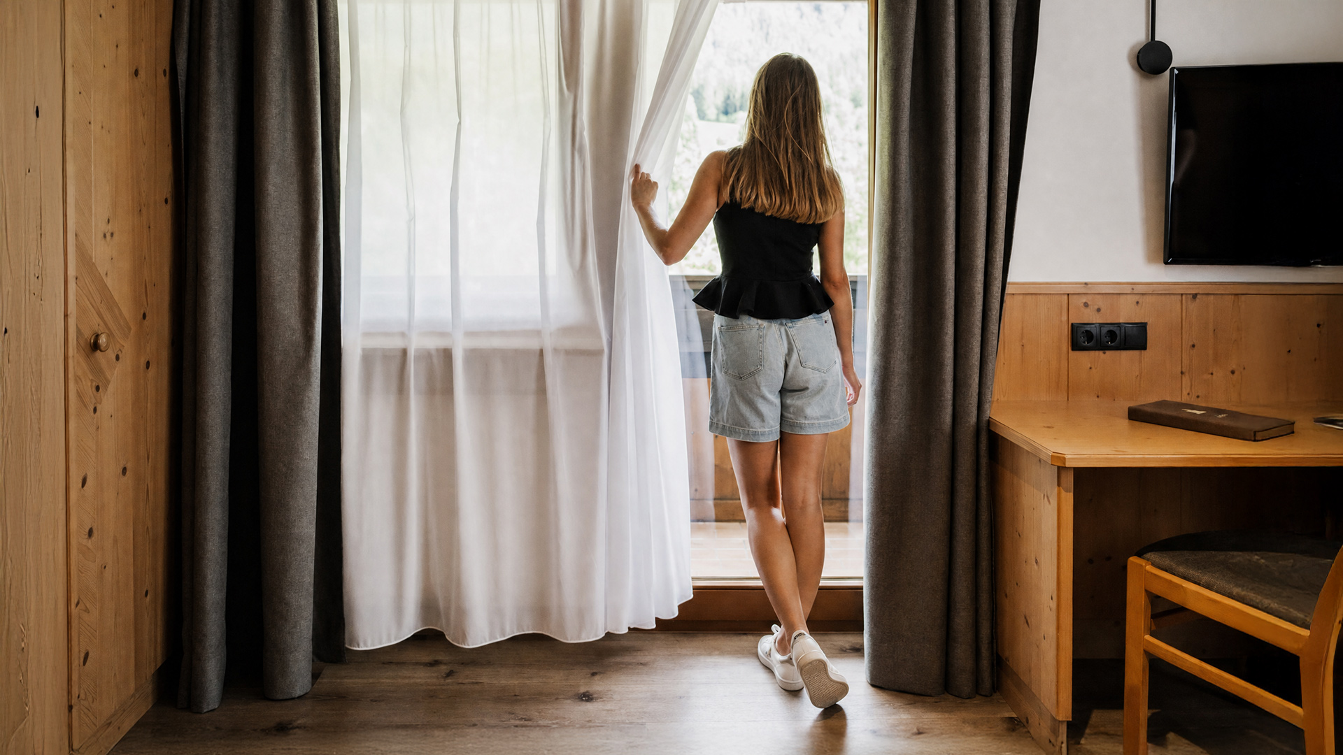 Una donna si trova nella stanza dell'Hotel Tannenhof, alza la tenda e guarda fuori dalla finestra.