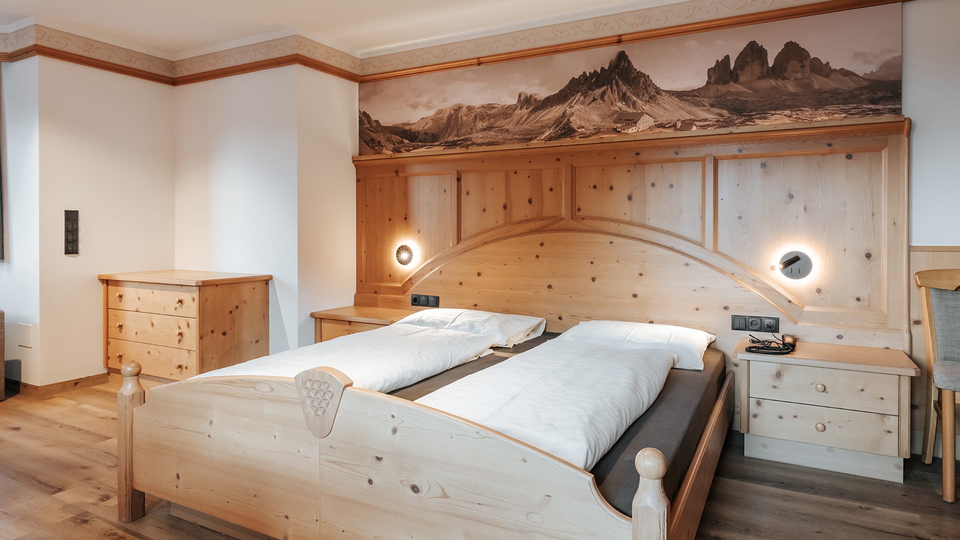 Un'accogliente camera matrimoniale all'Hotel Tannenhof al Kronplatz con legno chiaro, murale con vista sulle montagne e letti comodi.