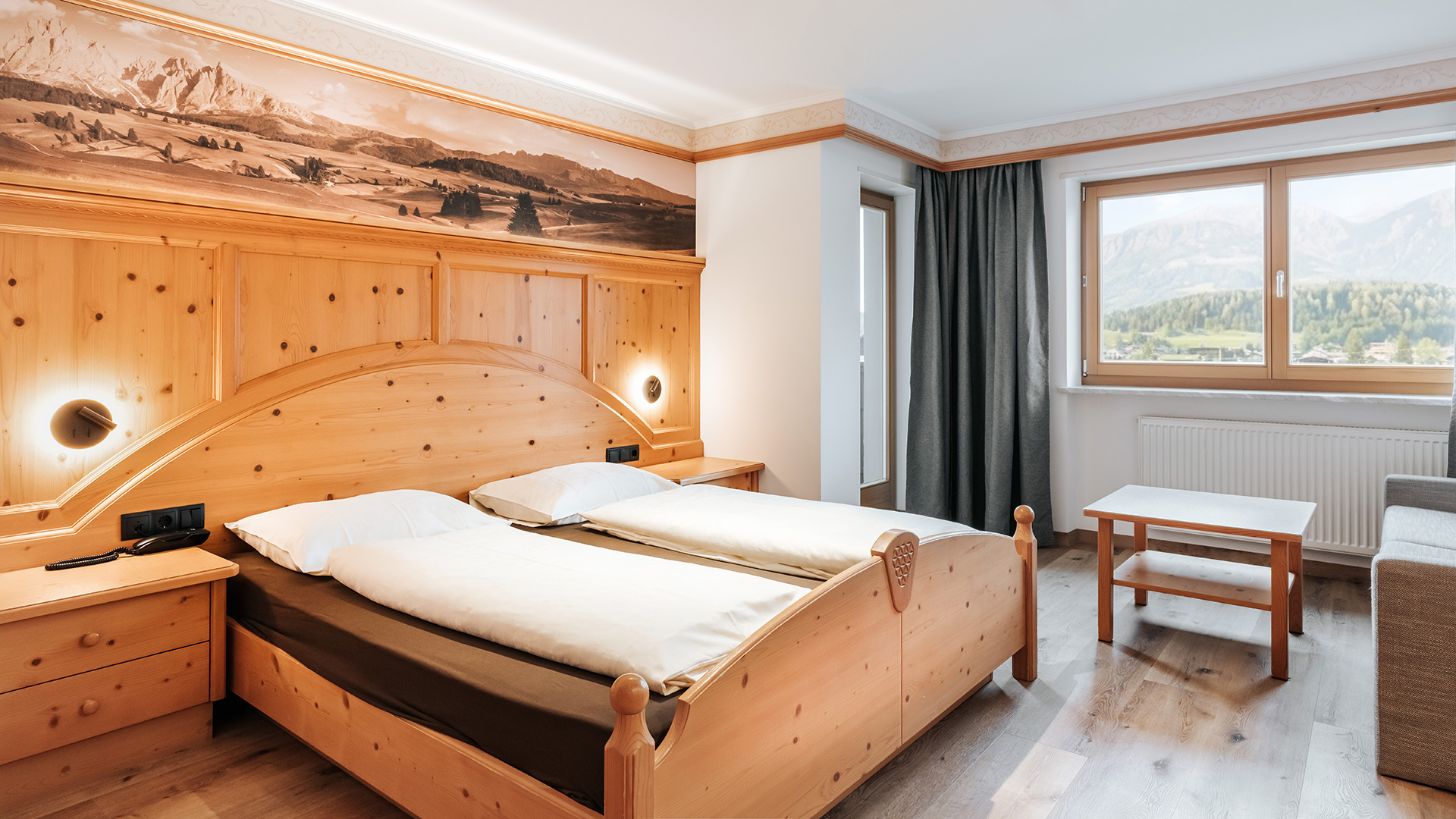 Accogliente camera matrimoniale nell'Hotel Tannenhof con interni in legno chiaro e vista sulle montagne del Kronplatz.