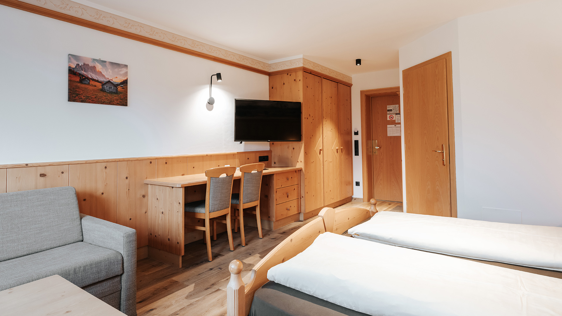 Accogliente camera doppia nell'Hotel Tannenhof con legno chiaro, scrivania, TV e due letti singoli.