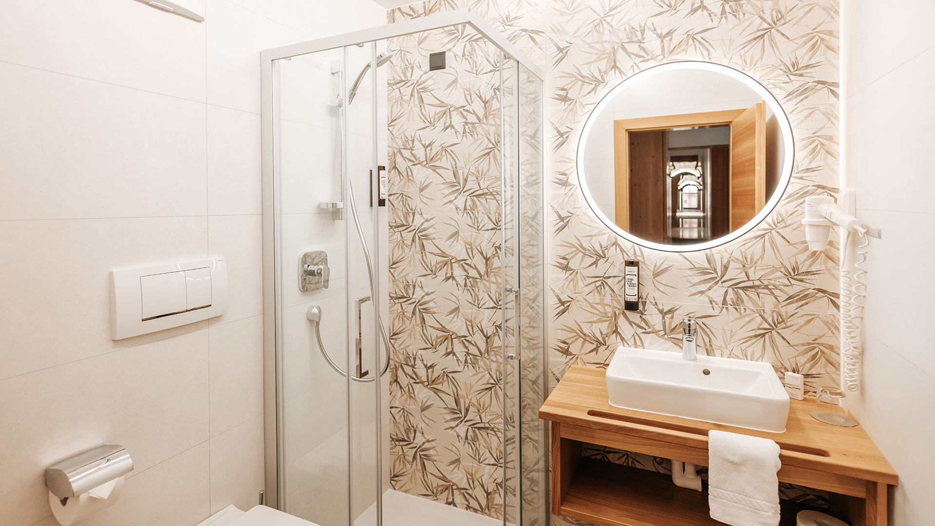 Bagno moderno nell'Hotel Tannenhof con cabina doccia, lavabo in legno e specchio illuminato.