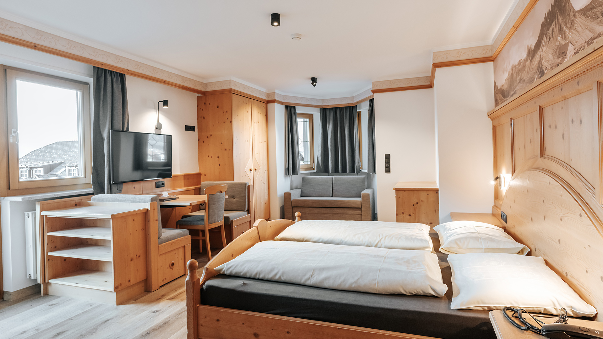 Spaziosa camera familiare nell'Hotel Tannenhof con letto matrimoniale, divano, tavolo da pranzo e vista sulle montagne.