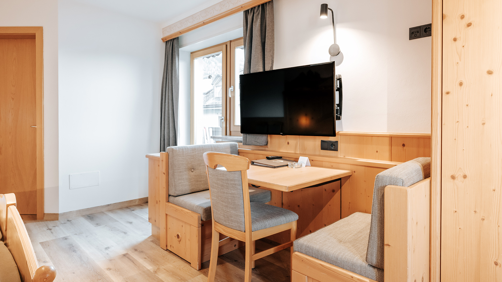 Accogliente camera familiare nell'Hotel Tannenhof con legno chiaro, tavolo da pranzo, panche, sedia e TV.