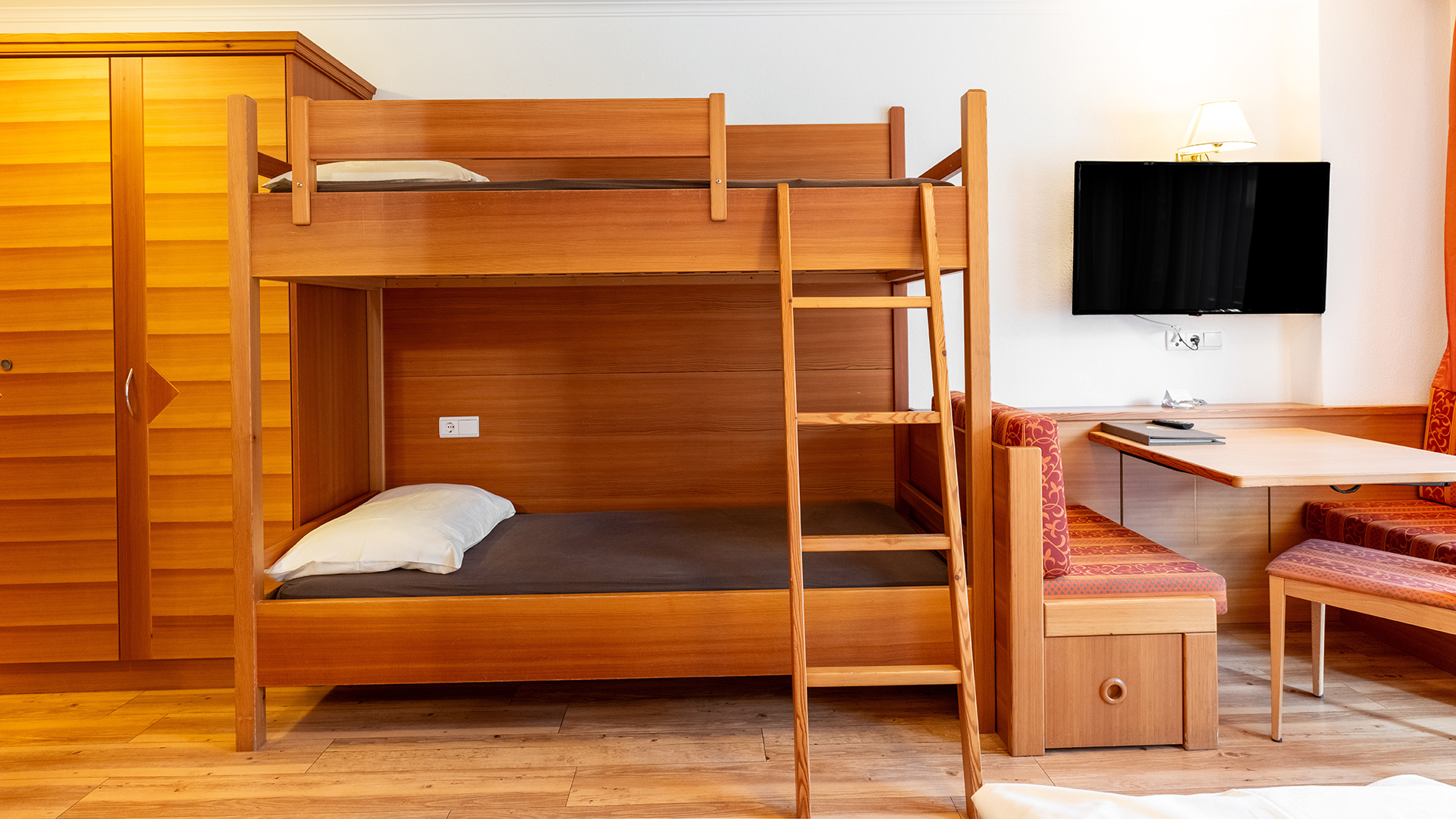 Accogliente camera familiare nell'Hotel Tannenhof con letto a castello in legno, armadio e angolo salotto con TV.