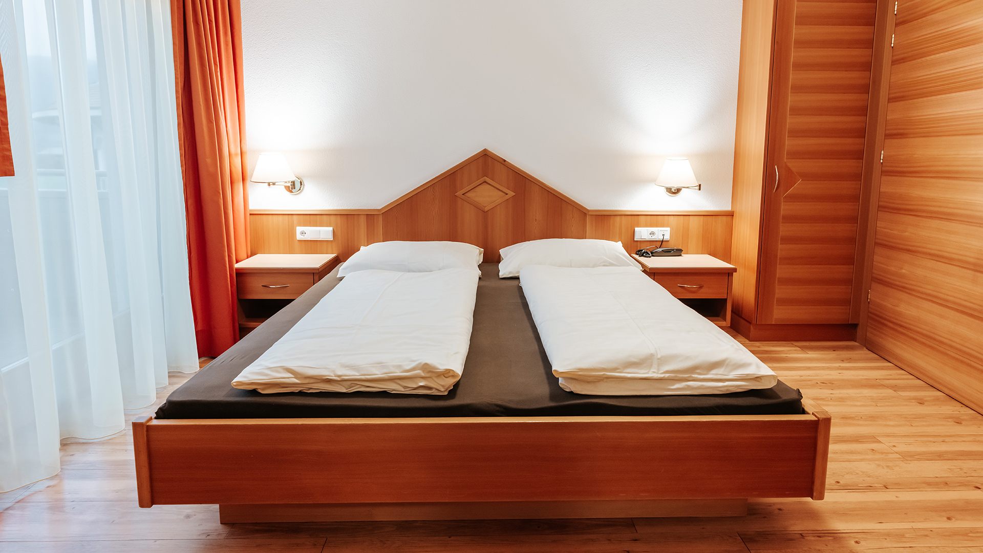 Accogliente camera matrimoniale nell'Hotel Tannenhof al Kronplatz, con elementi in legno e tende.