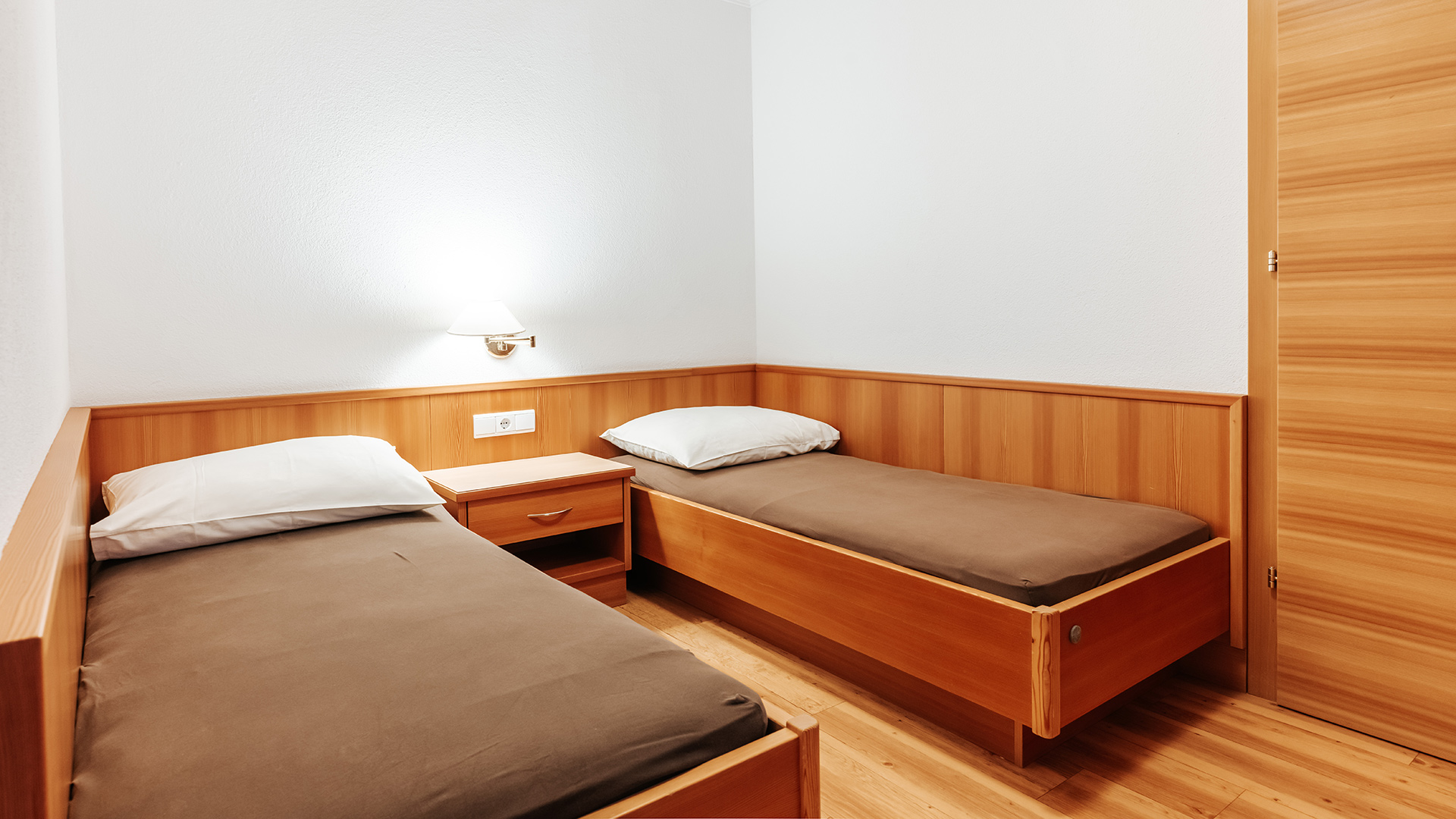 Accogliente camera familiare nell'Hotel Tannenhof con due letti singoli, mobili in legno e arredamento alpino.