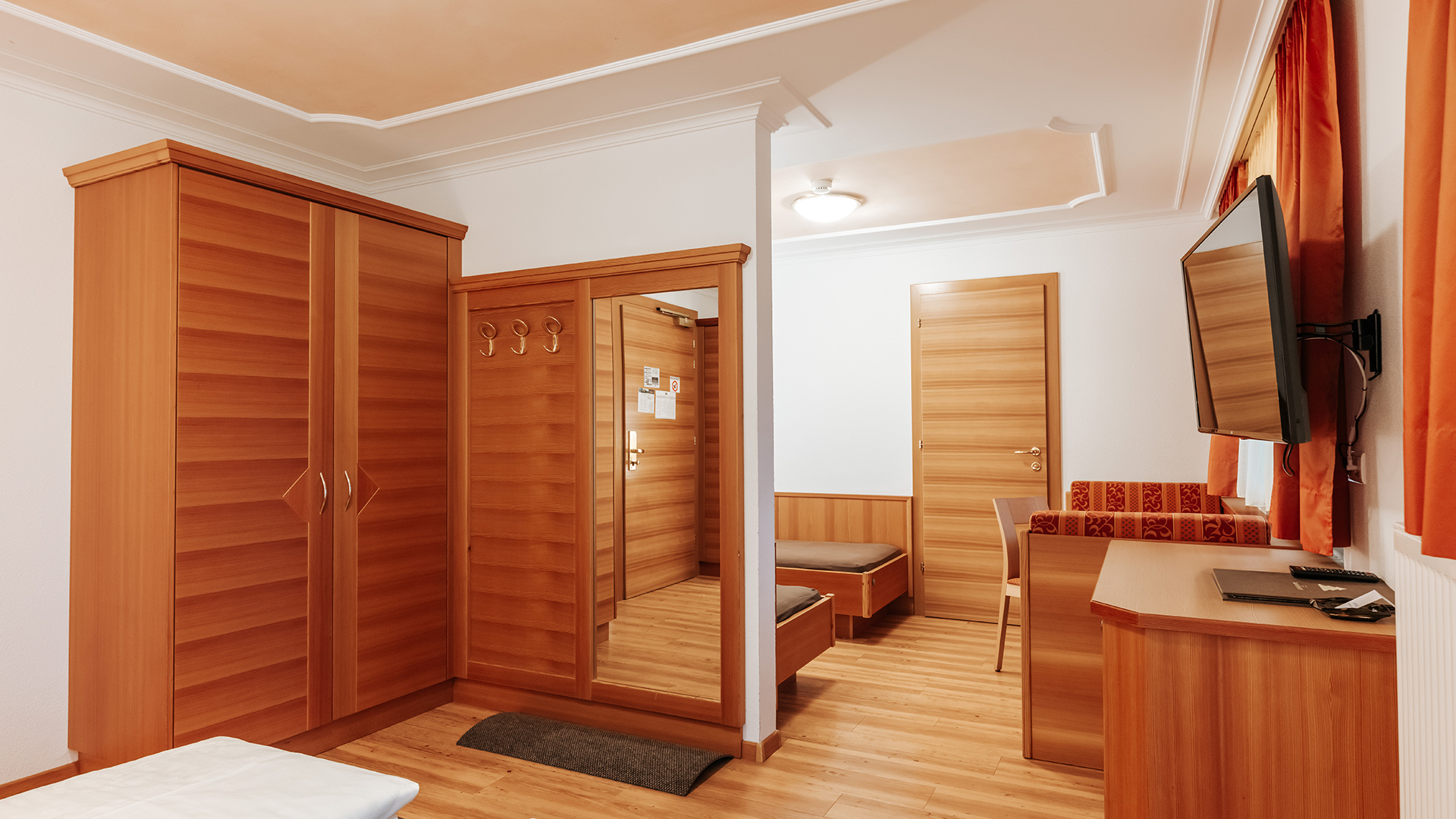 Accogliente camera familiare all'Hotel Tannenhof am Kronplatz con mobili in legno, armadio, specchio e TV.