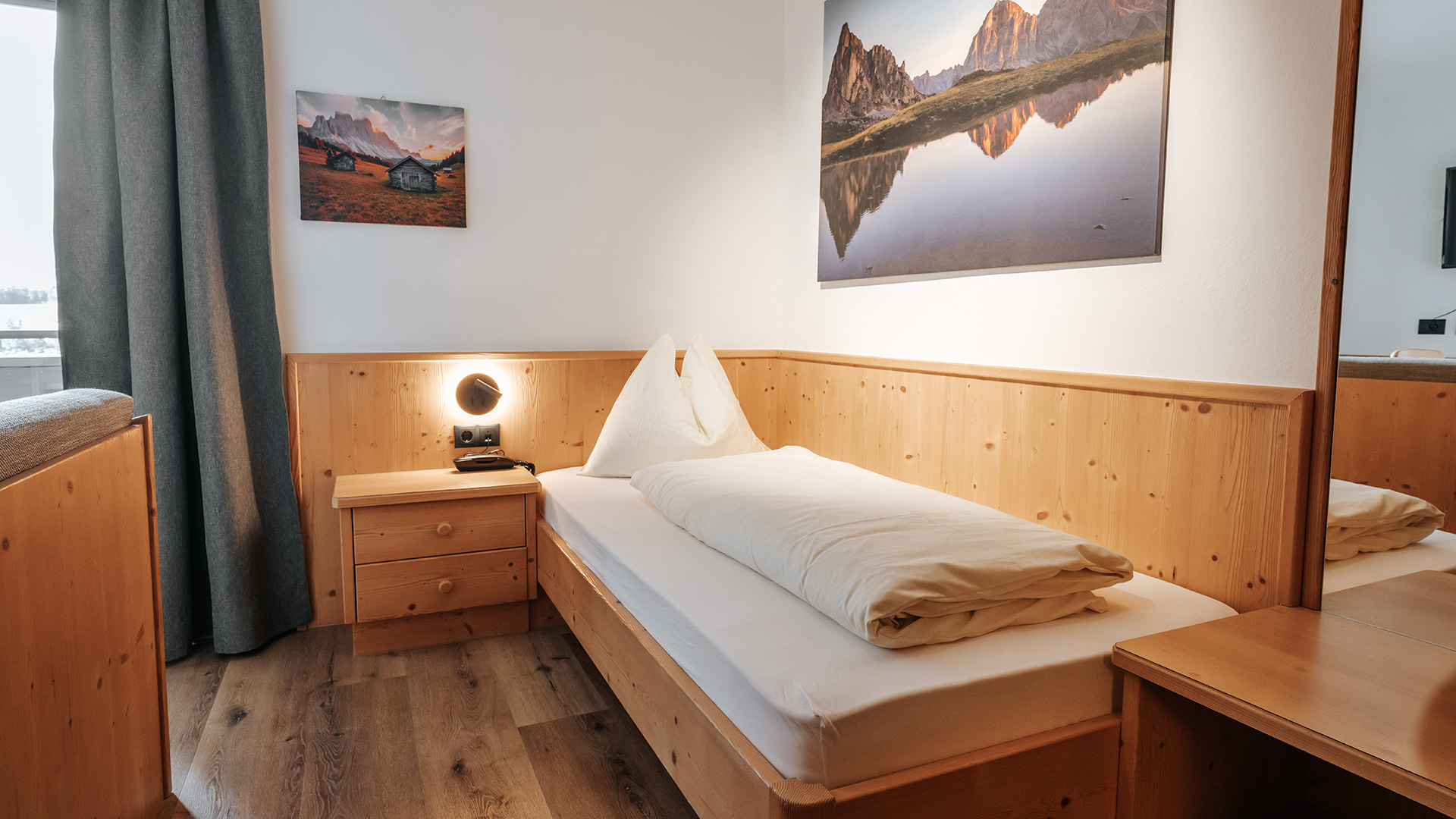 Accogliente camera singola all'Hotel Tannenhof am Kronplatz con legno chiaro, letto comodo e immagini di montagna.