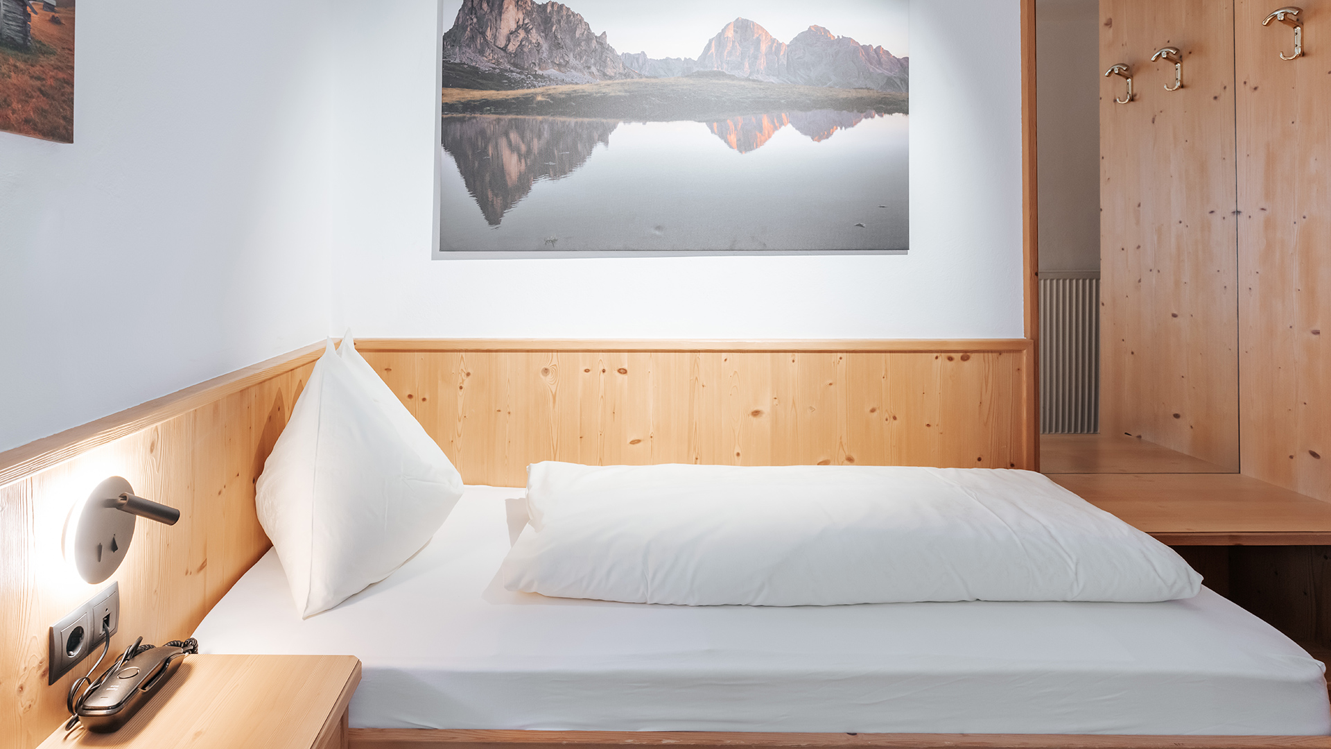 Accogliente camera singola all'Hotel Tannenhof am Kronplatz con legno chiaro, letto comodo e quadro di montagna.