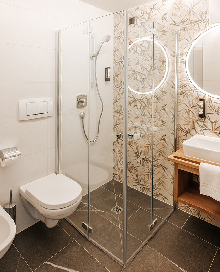 Bagno moderno nell'Hotel Tannenhof con doccia walk-in, WC e specchio illuminato.