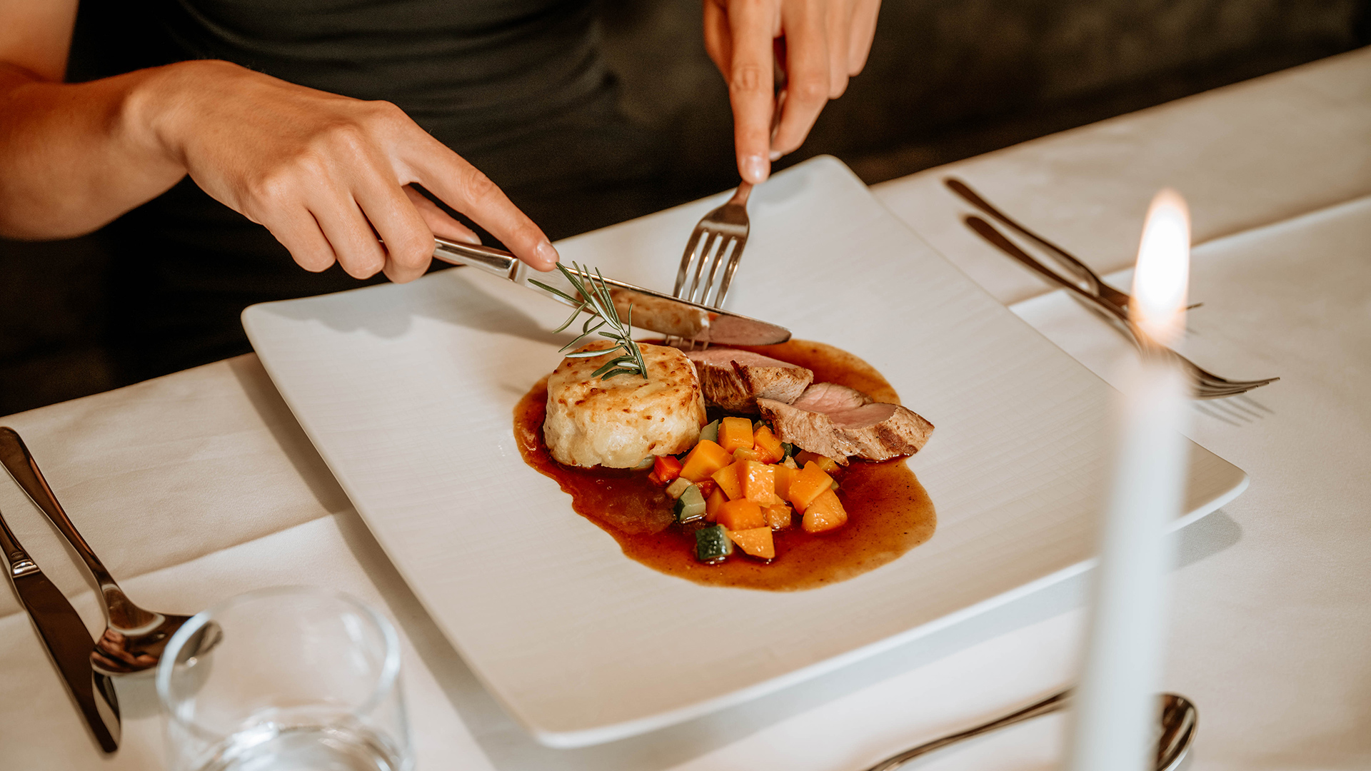 Primo piano di una persona che gusta un piatto festivo con carne, verdure e patate a lume di candela in un ristorante d'albergo.