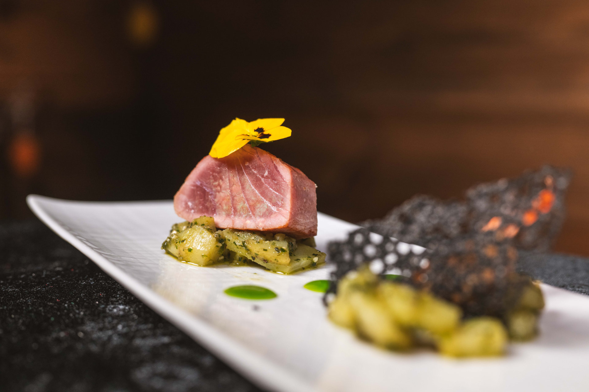 Un piatto artisticamente preparato con tonno scottato rosa su insalata di patate e un fiore giallo, servito all'Hotel Tannenhof.
