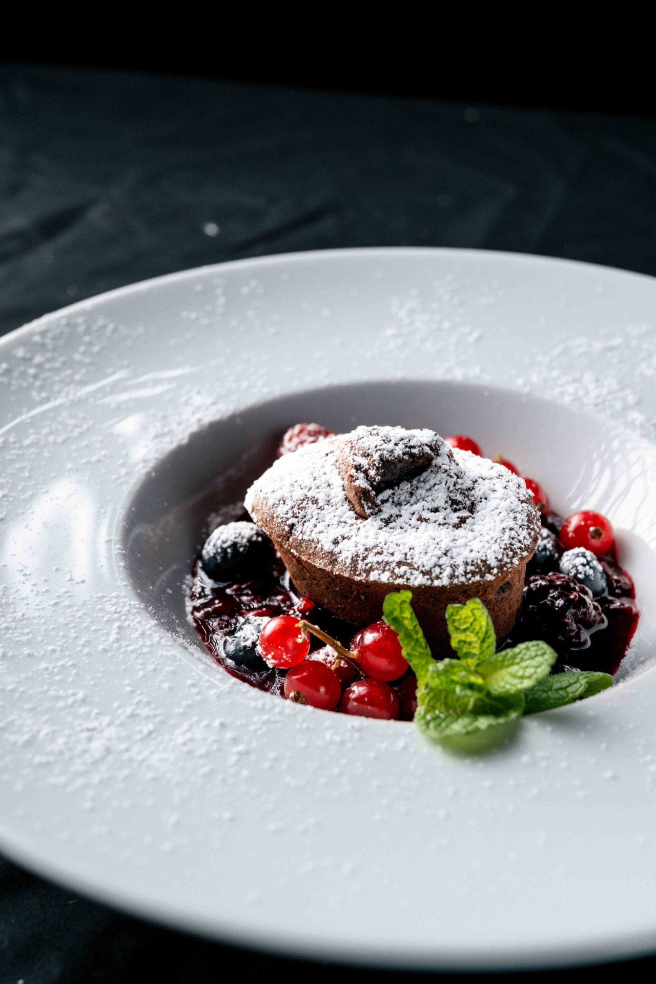 Un delizioso tortino al cioccolato con cuore morbido, spolverato di zucchero a velo, con frutti di bosco e menta, servito all'Hotel Tannenhof.