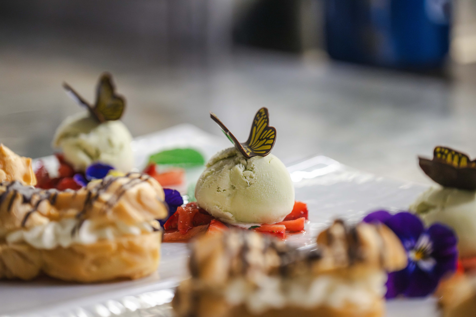 Primo piano di tre palline di gelato al pistacchio con decorazioni a farfalla, fragole e bignè.