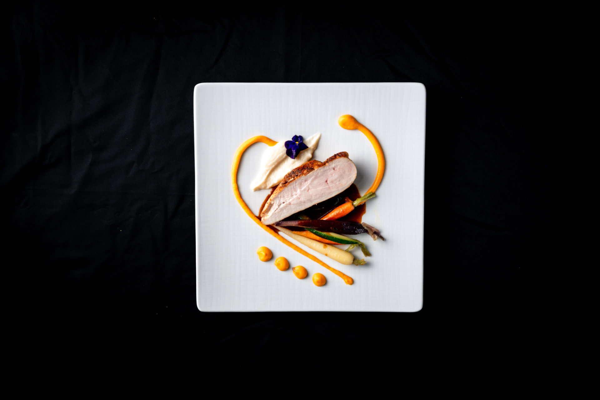 Un piatto artisticamente presentato con carne arrosto, carote colorate e salsa su un piatto bianco, che mostra la cucina gourmet dell'Hotel Tannenhof a Reischach.