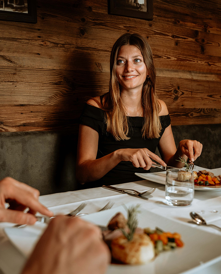 Una donna sorridente si gode una cena festiva con specialità regionali altoatesine all'Hotel Tannenhof.