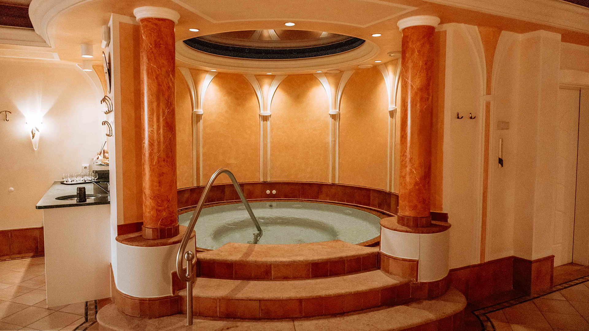 Einladender Whirlpool im Wellnessbereich des Hotel Tannenhof mit Stufen, Säulen und indirekter Beleuchtung.