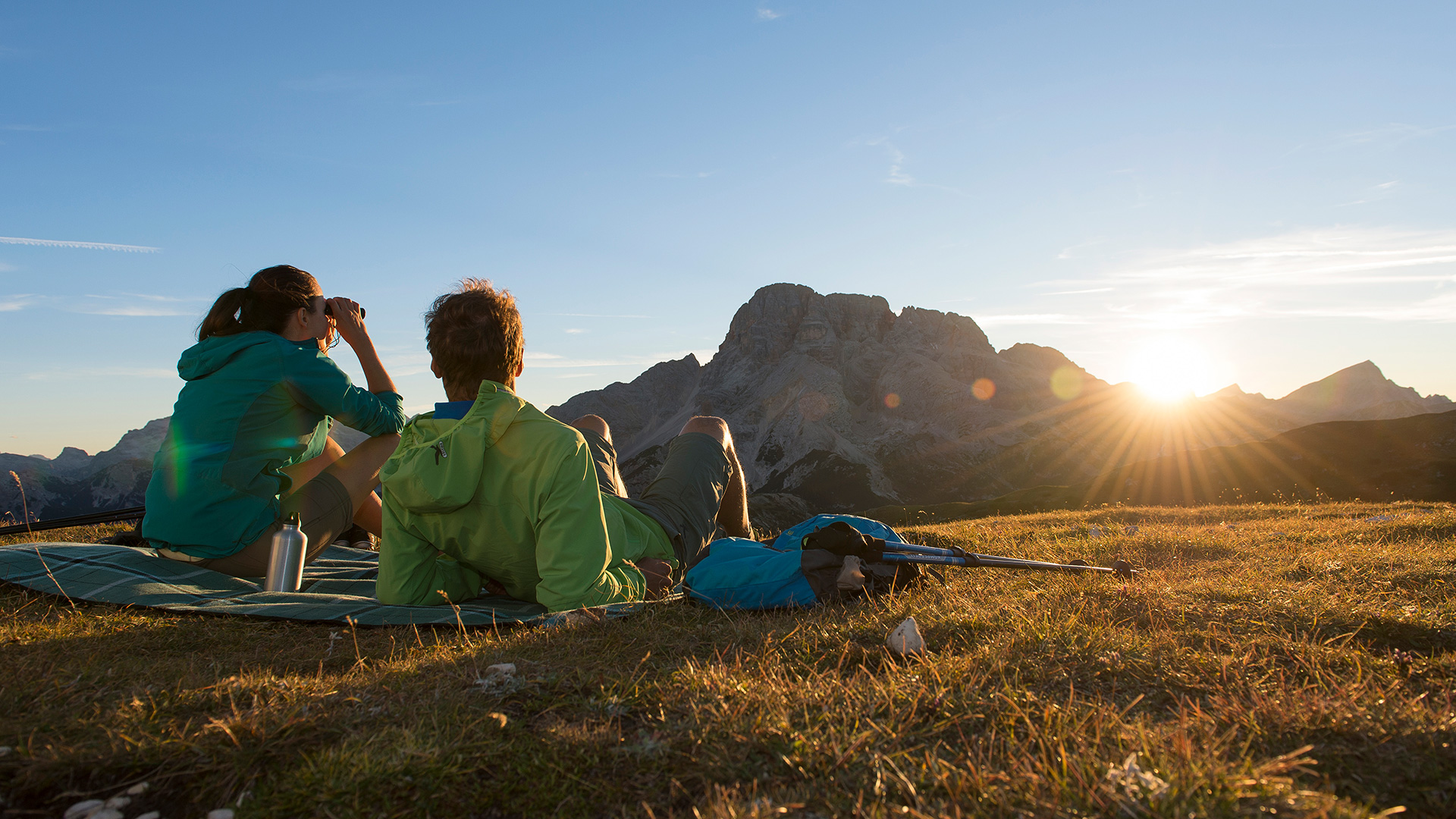 Zwei Wanderer genießen den Sonnenuntergang über den Bergen im Pustertal, ideal für Ihren Sommerurlaub.