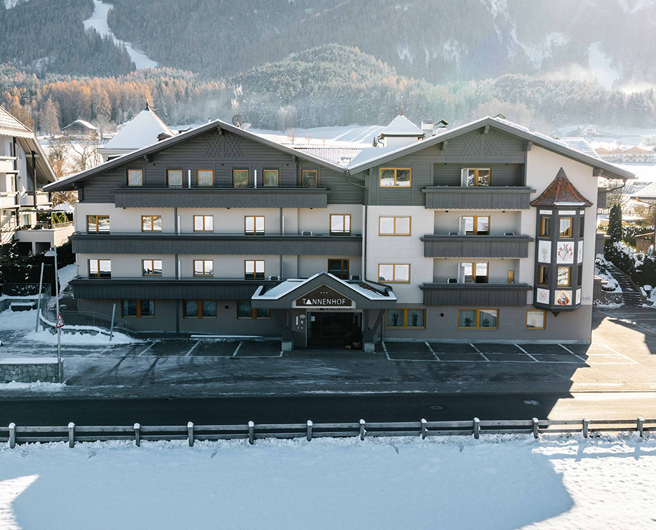 The Hotel Tannenhof in Reischach am Kronplatz in winter, surrounded by snow and mountains.